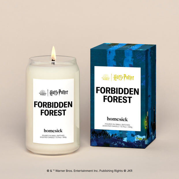 A lit Forbidden Forest Homesick candle displayed next to its boxed packaging on a dark cream background.