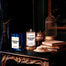 A lit Forbidden Forest Homesick candle displayed next to its boxed packaging decorative background with several props.