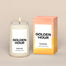 A lit Golden Hour Homesick candle displayed next to its boxed packaging on a dark cream background.