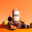 A lit Golden Hour Homesick candle on a rock surrounded by various fruit.