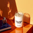 A lit Golden Hour Homesick candle on a desk next to a book and bottle of perfume.