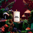 Lifestyle image of a candle surrounded by forest elements in a dark scene