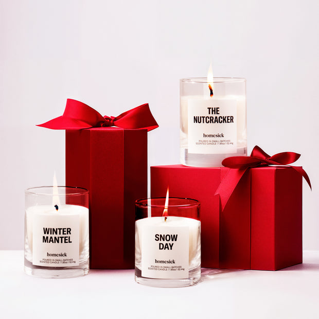 All three lit Winter Wonderland Mini Candles in front of and on top of presents on a white background.