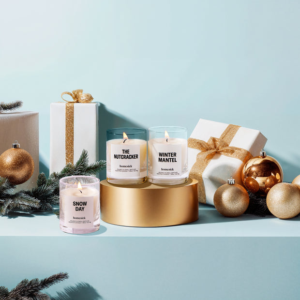 All three lit Winter Wonderland Mini Candles surrounded by presents and Christmas tree ornaments.