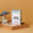 A Beach Cottage Candle inside a miniature play sandbox. The image was taken in a deep orange studio setting.