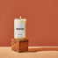 A Boston Homesick Candle displayed on top of a wooden cube. The cube is displayed on a cork surface and reddish background.