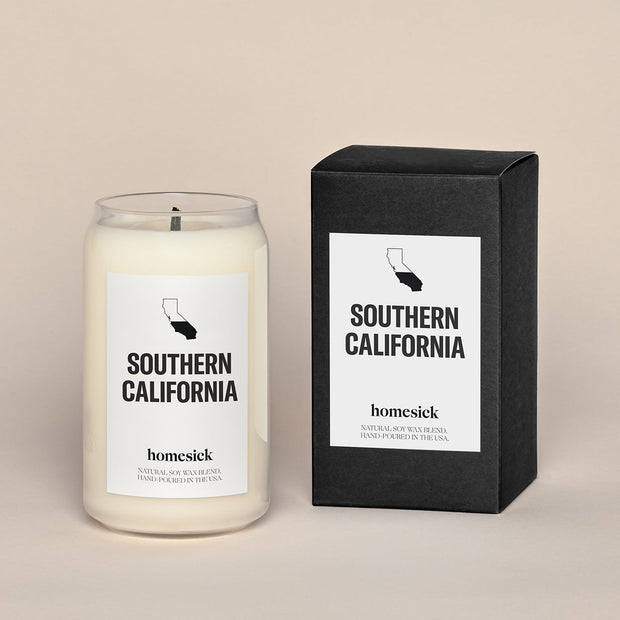 A lit Southern California Homesick candle displayed next to its boxed packaging on a dark cream background.