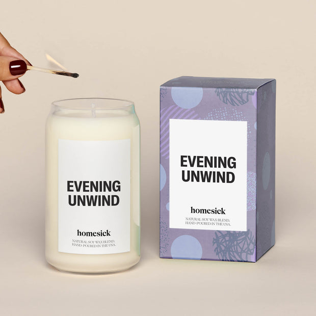 Single evening unwind lit candle next to a purple box, which the candle comes in.