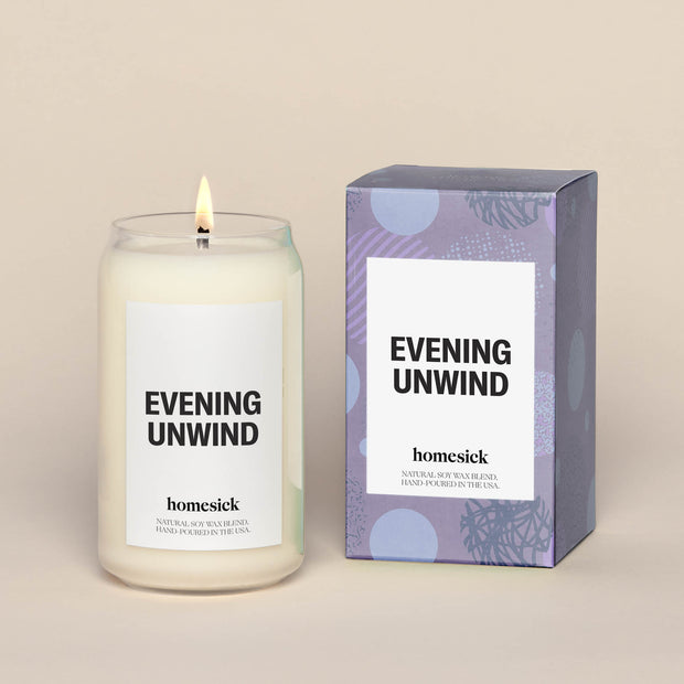 Single evening unwind lit candle next to a purple box, which the candle comes in.