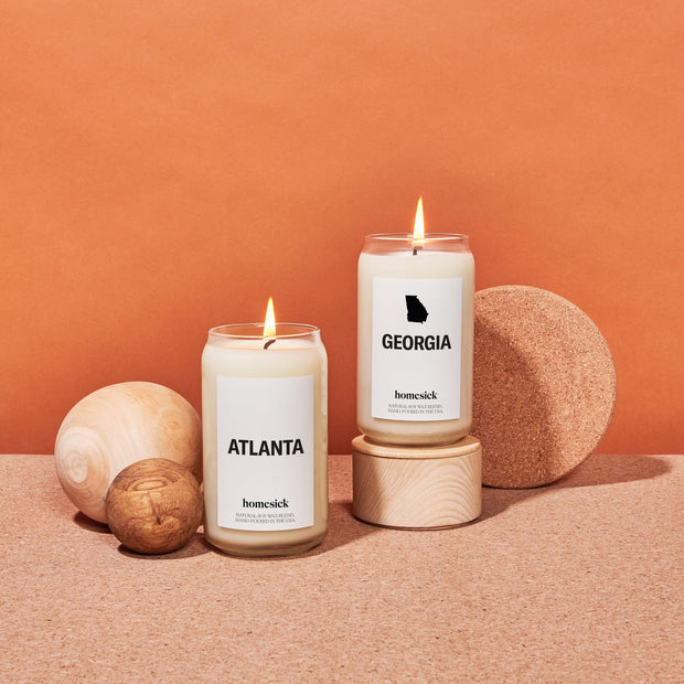 The Atlanta and Georgia homesick candles shot in an abstract art inspired environment. The surface is a corkboard and the background in a deep orange.