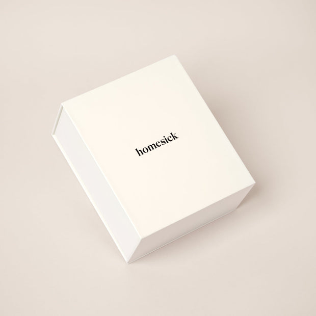 A white candle box that displays how a candle fits perfectly inside. The top lid packaging reads, "where the heart is" and inside is the Let's Toast candle.