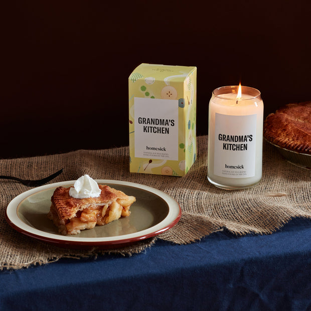 A stylized shot of the Grandma's Kitchen candle next to it's packaging. There is a nice slice of apple pie in the shot.