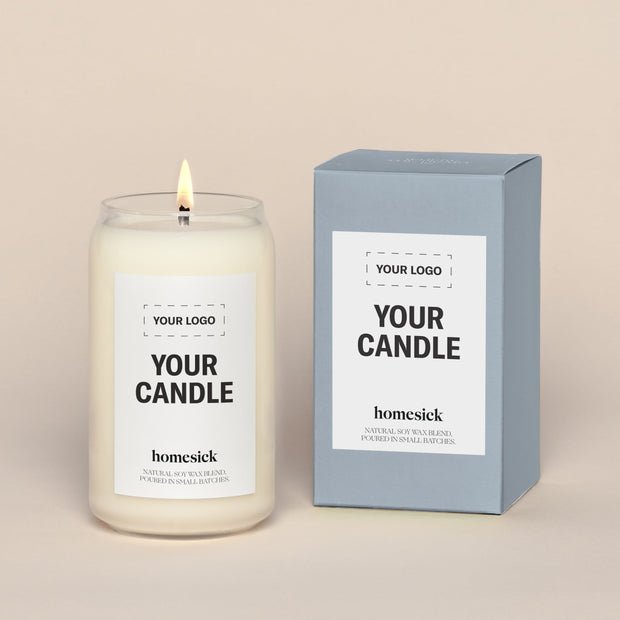 A generic Homesick candle that is lit. The candle label and its packaging display where a customized logo can be added.