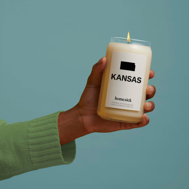 A hand holding the Kansas candle over a blueish green background.