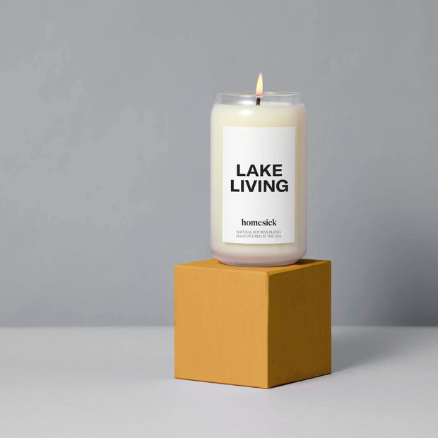 A dark mustard cube pedestal with the Lake Living Candle on top. The items are shot in a gray studio environment.