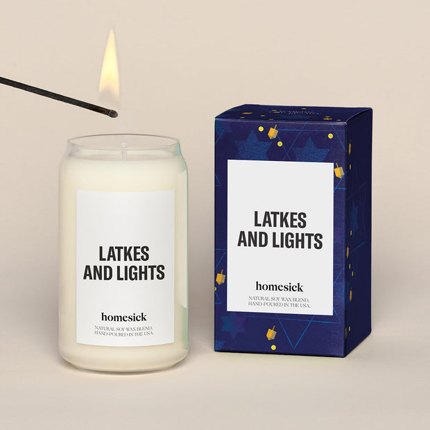 A lit Latkes and Lights Homesick candle displayed next to its boxed packaging on a dark cream background.