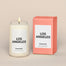 A lit Los Angeles Homesick candle displayed next to its boxed packaging on a dark cream background.