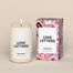 A lit Love Letters Homesick candle displayed next to its boxed packaging on a dark cream background.