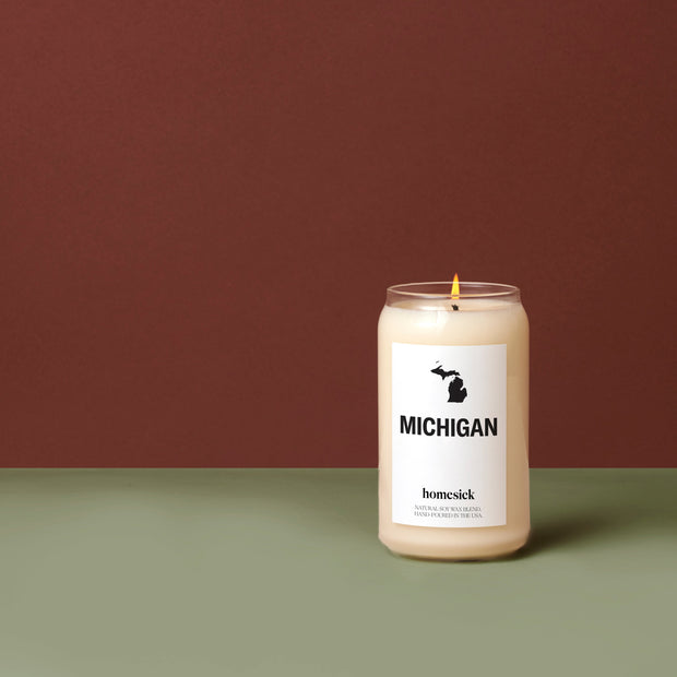 A lit Michigan Candle displayed on a deep mint green surface in front of a deep ruby background.