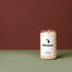 A lit Michigan Candle displayed on a deep mint green surface in front of a deep ruby background.