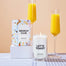 Two of Homesicks Candles on top of a light blue checkered tablecloth with two glasses of mimosas.