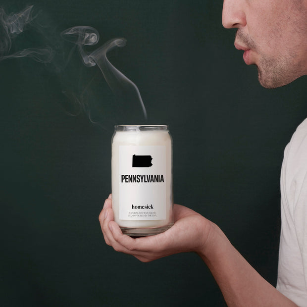 A model holding the Pennsylvania candle in front of a deep emerald background. They just blew out the candle so there is smoke in the air.