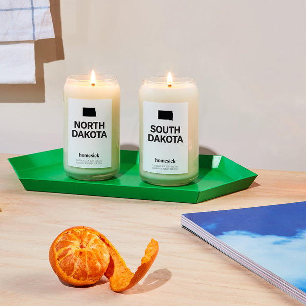 The North and South Dakota candles on a green hexagonal tray that sits on a light wood surface.