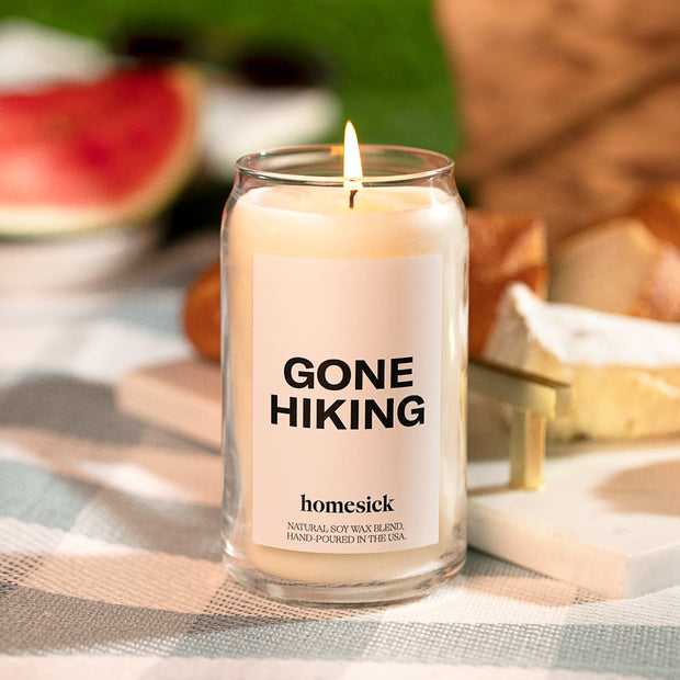 A close up of the Gone Hiking candle. The background is blurred but one can decipher a picnic.