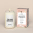 A lit Team Homesick candle displayed next to its boxed packaging on a dark cream background. The boxed packaging is turned aroud and shows the custom message.