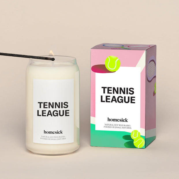 A lit Tennis League Homesick candle displayed next to its boxed packaging on a dark cream background.