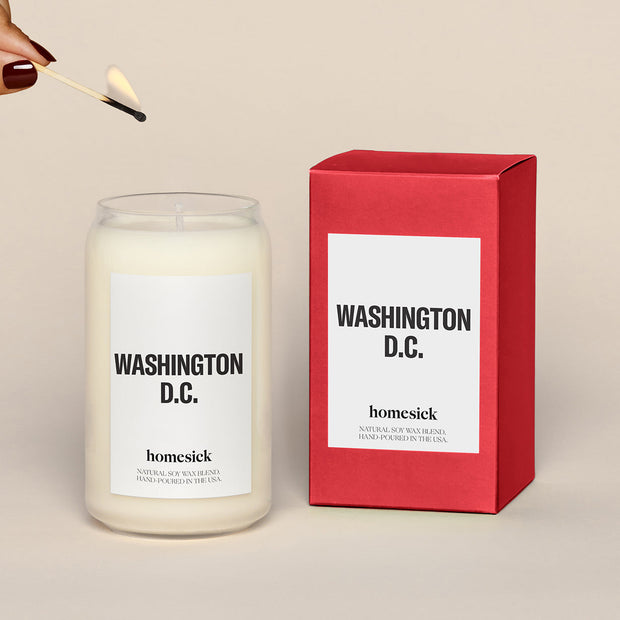 A lit Washington, D.C. Homesick candle displayed next to its boxed packaging on a dark cream background.