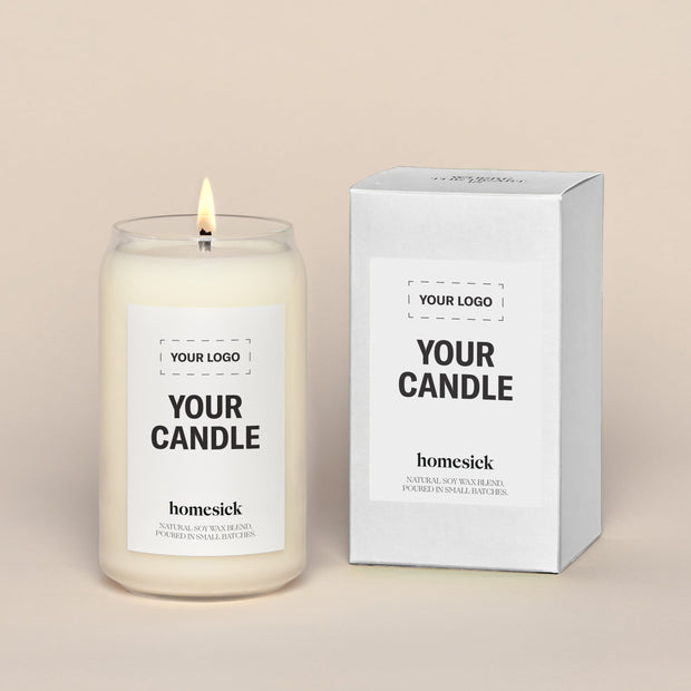 A generic Homesick candle that is lit. The candle label and its packaging display where a customized logo can be added.