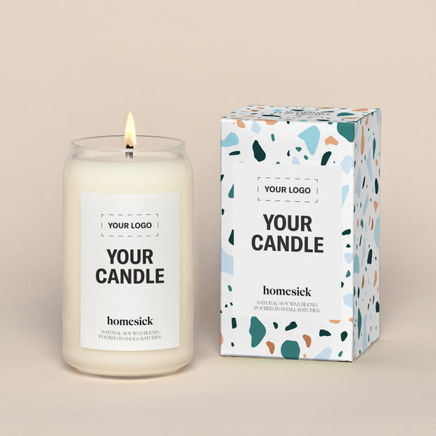 A generic Homesick candle that is lit. The candle label and its packaging display where a customized logo can be added.