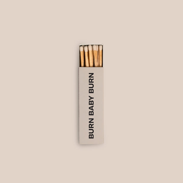 Three boxes of Homesick matches shot on a dark cream background. Two boxes are stacked while the third box is slight displayed open.