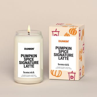 A lit candle displayed next to its boxed packaging on a dark cream background.