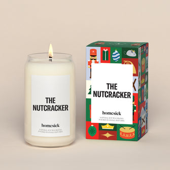 A lit Nutcracker Homesick candle displayed next to its boxed packaging on a dark cream background.