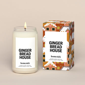 A lit Gingerbread House Homesick candle displayed next to its boxed packaging on a dark cream background.