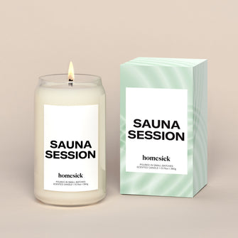 A lit Homesick Sauna Session candle and its box on a cream background