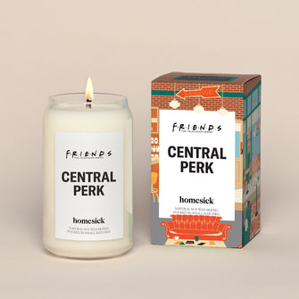 A lit Central Park Homesick candle displayed next to its boxed packaging on a dark cream background.