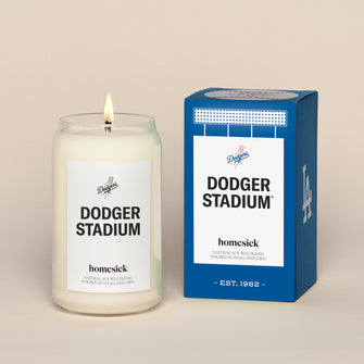 A lit Dodger Stadium Homesick candle displayed next to its boxed packaging on a dark cream background.