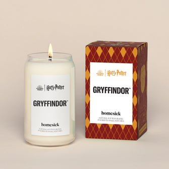 A lit Gryffindor Homesick candle displayed next to its boxed packaging on a dark cream background.