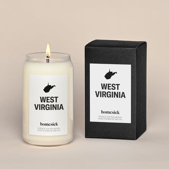 A lit West Virginia Homesick candle displayed next to its boxed packaging on a dark cream background.